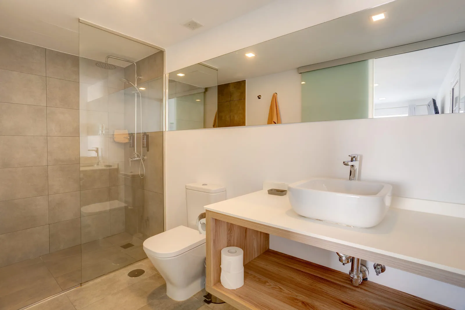 El baño, con ducha a ras de suelo tras una mampara y lavabo sobre una repisa de madera abierta