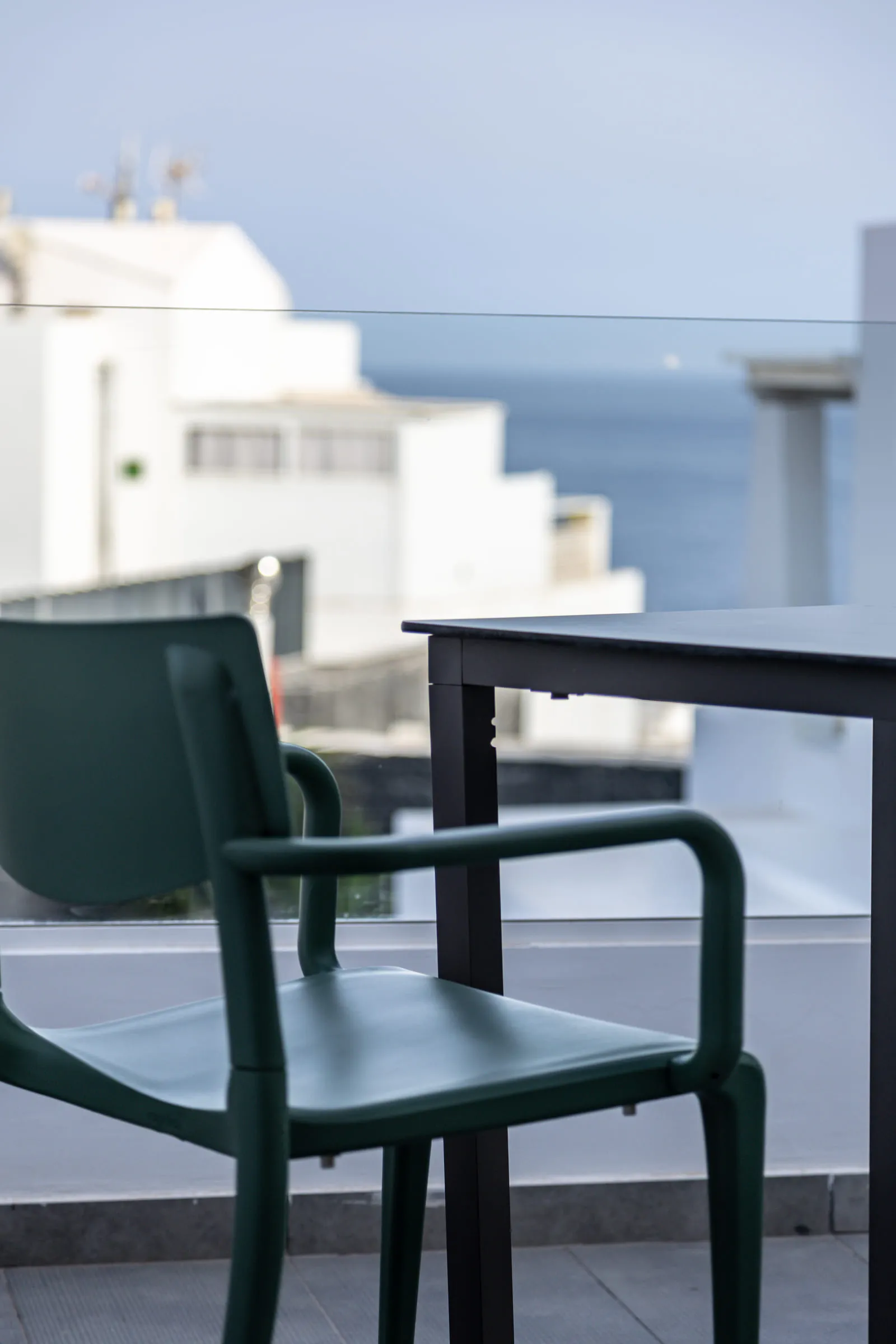 Una silla y una mesa en la terraza, y más allá el mar tras la barandilla de cristal